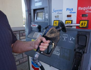 Hand o the gas pump nozzle ready to choose fuel type to refill vehicle.