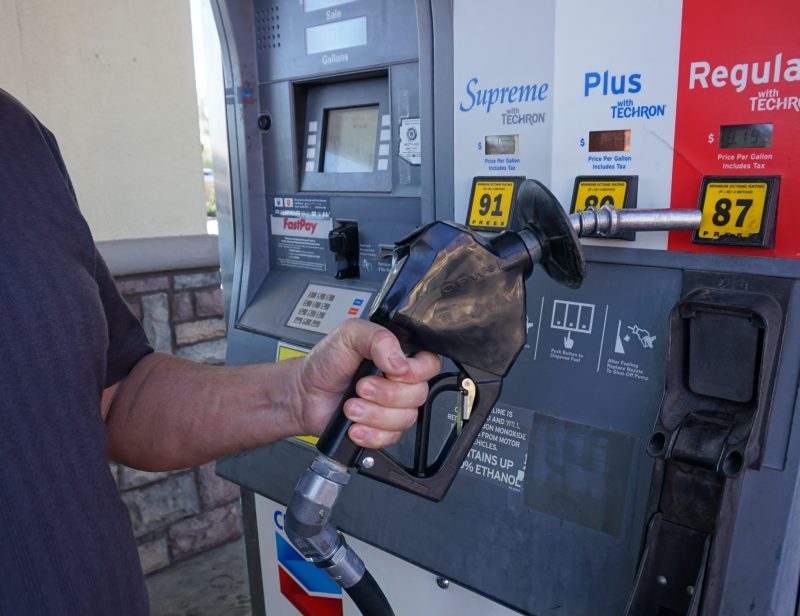 Hand o the gas pump nozzle ready to choose fuel type to refill vehicle.