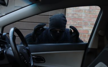 Thief wearing black and looking in through a car window.