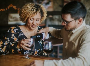 A man pours wine for a woman while they sit together in a winery.