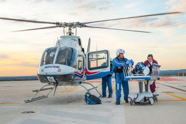 Two emergency care workers take a patient to a helicopter via stretcher.