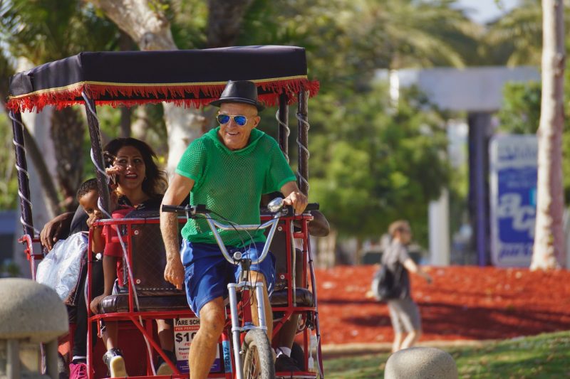 Happy pedicab driver and his passengers on a sunny day outside in the park.