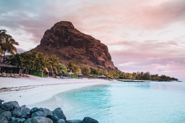 Beautiful turquoise ocean coast at dusk, tall rocks along the shore of the white sandy beach.