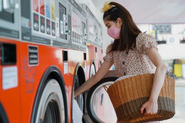 New normal lifestyle, Asian beautiful millennial woman washing her clothes in the automatic laundry self service