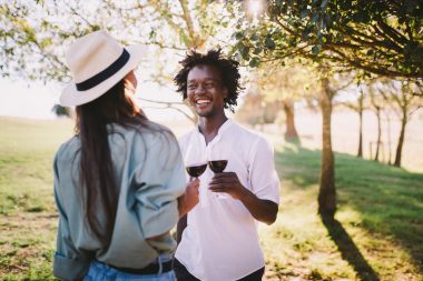 Young man and woman enjoy a summer day in a vineyard with glasses of wine.