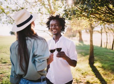 Young man and woman enjoy a summer day in a vineyard with glasses of wine.