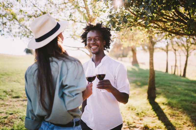 Young man and woman enjoy a summer day in a vineyard with glasses of wine.
