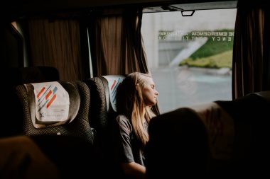 A woman leans her head towards the window to sleep while she travels on a bus.