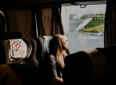 A woman leans her head towards the window to sleep while she travels on a bus.