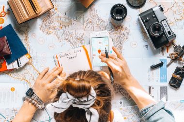 Top down view of travel planning with a notebook, phone, camera, and map.