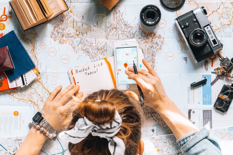 Top down view of travel planning with a notebook, phone, camera, and map.