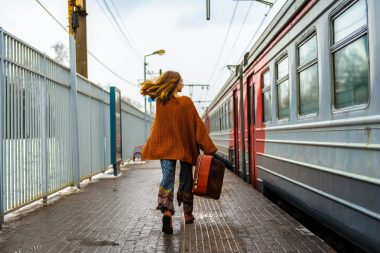 Woman walks alongside a train carrying a suitcase.