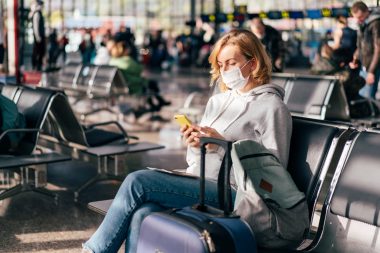 A woman in a protective medical mask on her face sits at the airport waiting for a flight.