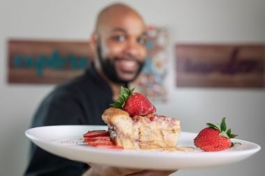 Cook holding up a plate of delicious cake and strawberries