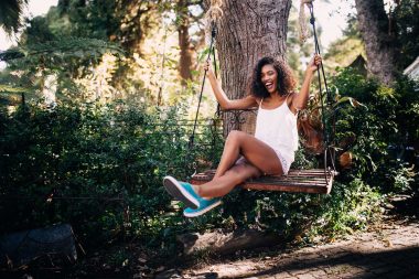 A happy mixed race woman swings on a wooden garden swing and enjoys the outdoors.