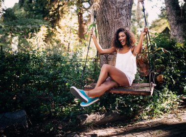 A happy mixed race woman swings on a wooden garden swing and enjoys the outdoors.