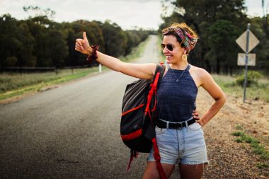 a woman hitchikes with a backpack on a rural road