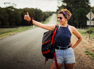 a woman hitchikes with a backpack on a rural road