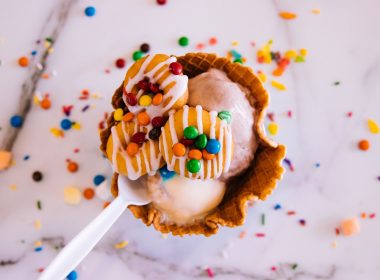 A waffle cone bowl with big scoops of chocolate ice cream and m&Ms and cookies on top.
