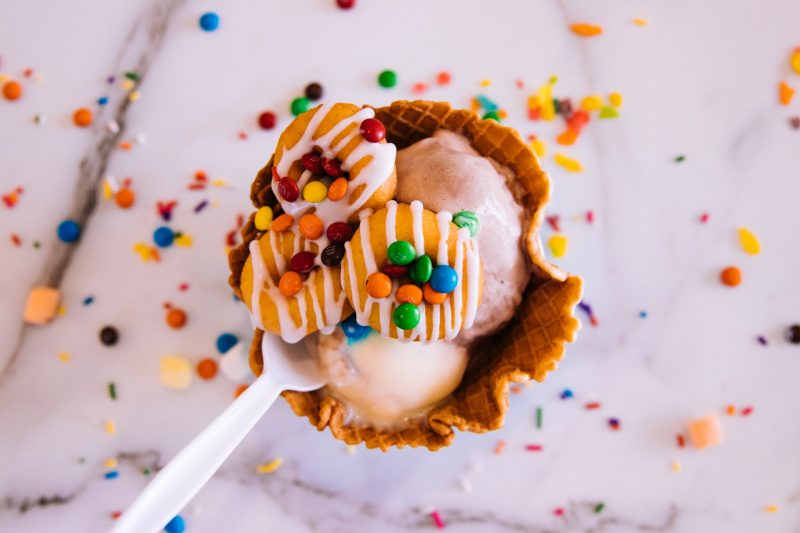 A waffle cone bowl with big scoops of chocolate ice cream and m&Ms and cookies on top.