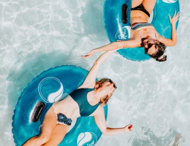 Two yougn women in bikinis floating in tubes on a lazy river in a water park.