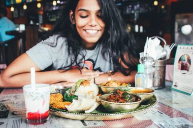 Woman with dark hair smiling and looking at a delicious plate of food at her table in a restaurant.