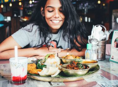 Woman with dark hair smiling and looking at a delicious plate of food at her table in a restaurant.
