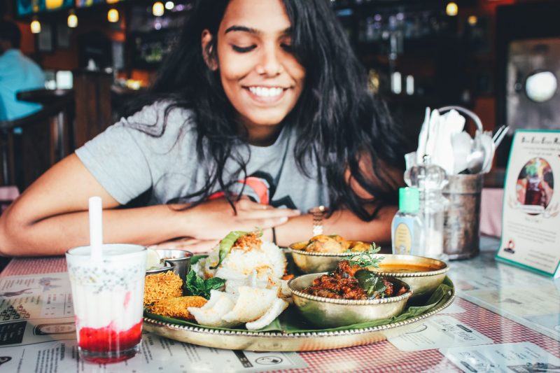 Woman with dark hair smiling and looking at a delicious plate of food at her table in a restaurant.