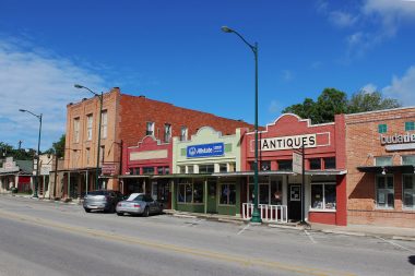 Shops along the street in historic downtown Buda, TX on a blue sky, sunny day.