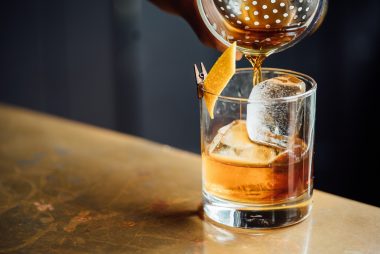 Pouring a whiskey drink over ice on a bar top in a dimly lit