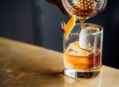 Pouring a whiskey drink over ice on a bar top in a dimly lit