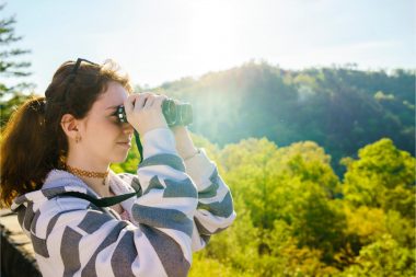 A young hiker looks through her binoculars while standing on high ground in Cherokee National Forest in Tennessee (TN).