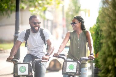 A couple enjoys a bike ride through a small town on a sunny summer day, laughing together.