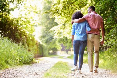A couple walking with their arms around each other down a dirt road in the countryside.