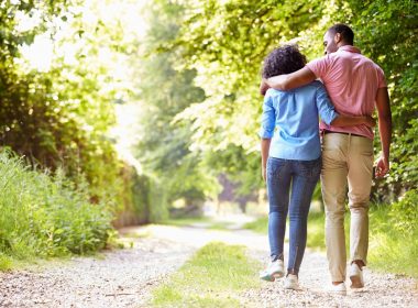A couple walking with their arms around each other down a dirt road in the countryside.