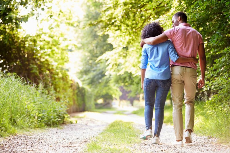 A couple walking with their arms around each other down a dirt road in the countryside.