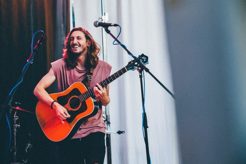 A musician performs on stage with his guitar and grins out to the audience