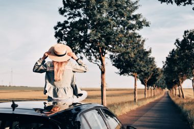 Rear view of woman sitting on the car at sunset on a road trip