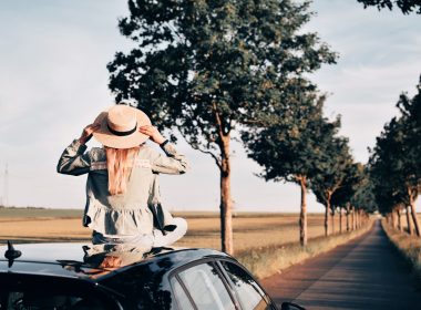 Rear view of woman sitting on the car at sunset on a road trip
