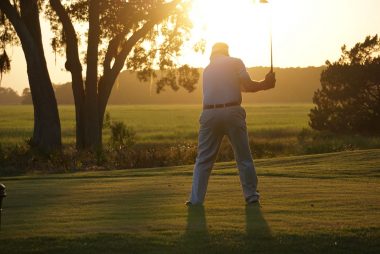 A golfer swings his club as he finishes his final hole on the course in the late summer sun.