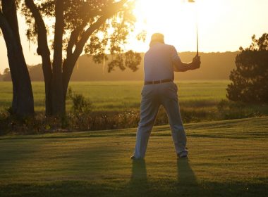 A golfer swings his club as he finishes his final hole on the course in the late summer sun.