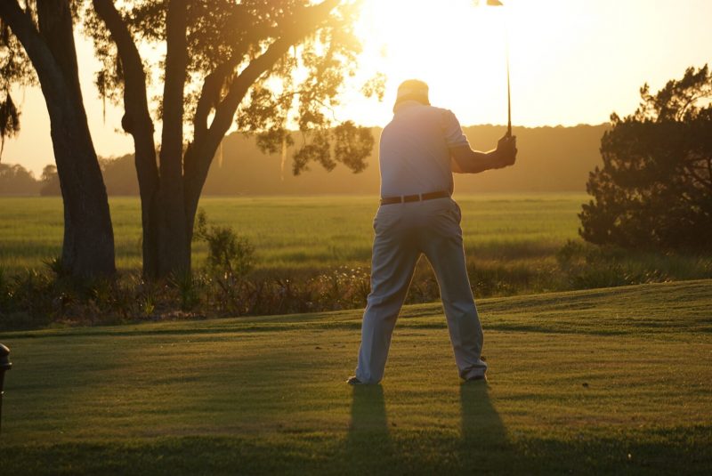 A golfer swings his club as he finishes his final hole on the course in the late summer sun.