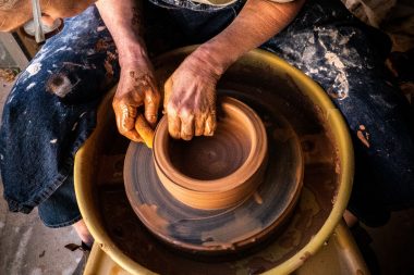 A woman bends over a pottery wheel and shapes a pot with a sponge.