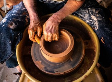 A woman bends over a pottery wheel and shapes a pot with a sponge.