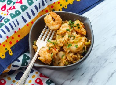 A bowl of fresh seafood shrimp jumbalaya in a bowl next to a colorful table cloth