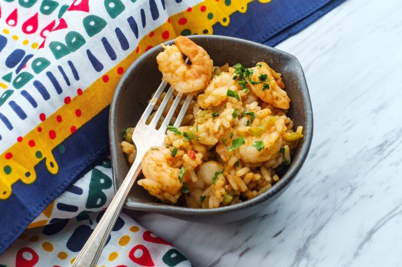 A bowl of fresh seafood shrimp jumbalaya in a bowl next to a colorful table cloth