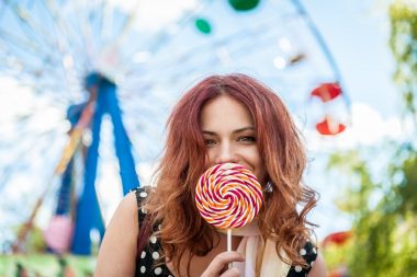 A red haired woman with an large old-fashioned lollipop held up over her mouth.