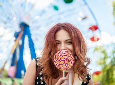 A red haired woman with an large old-fashioned lollipop held up over her mouth.