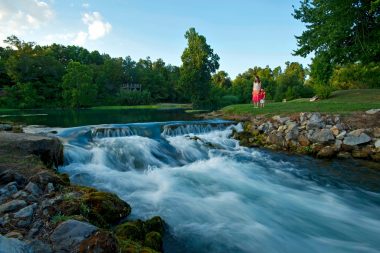 A mother and daughter hold hands and stand near the water's edge at Mammoth Spring in Cherokee Village, AR.