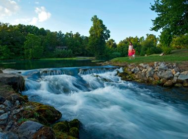 A mother and daughter hold hands and stand near the water's edge at Mammoth Spring in Cherokee Village, AR.